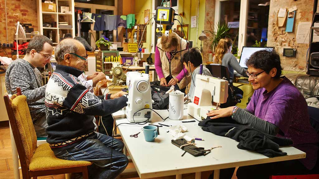 Mehrere Menschen sitzen an einem Tisch und reparieren technische Geräte. 